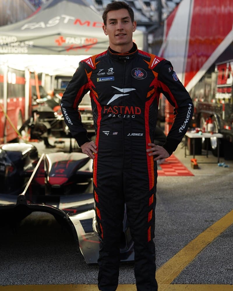 Driver wearing the finished black, red and grey FASTMD Racing Torq Superlight suit in the pit lane.
