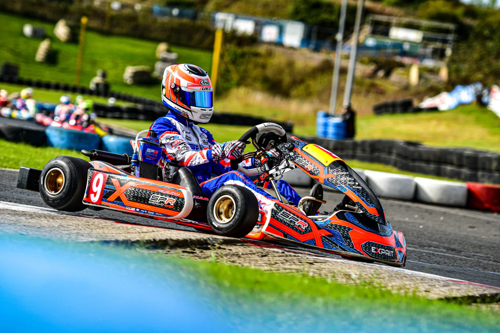Karter in a red, white and blue Torq suit driving kart number 9 through a circuit corner.