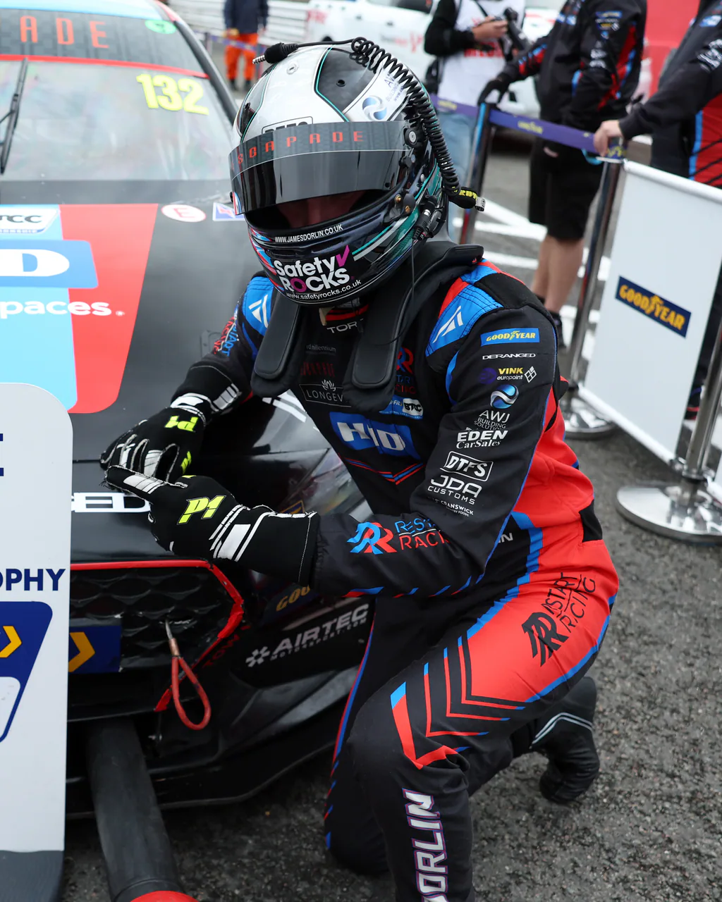 Helmeted driver in a black, blue and red Torq race suit celebrating beside a touring car and winner board.