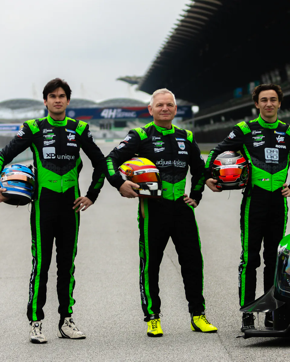 Three drivers in black and green Torq race suits standing with their helmets beside a prototype race car.