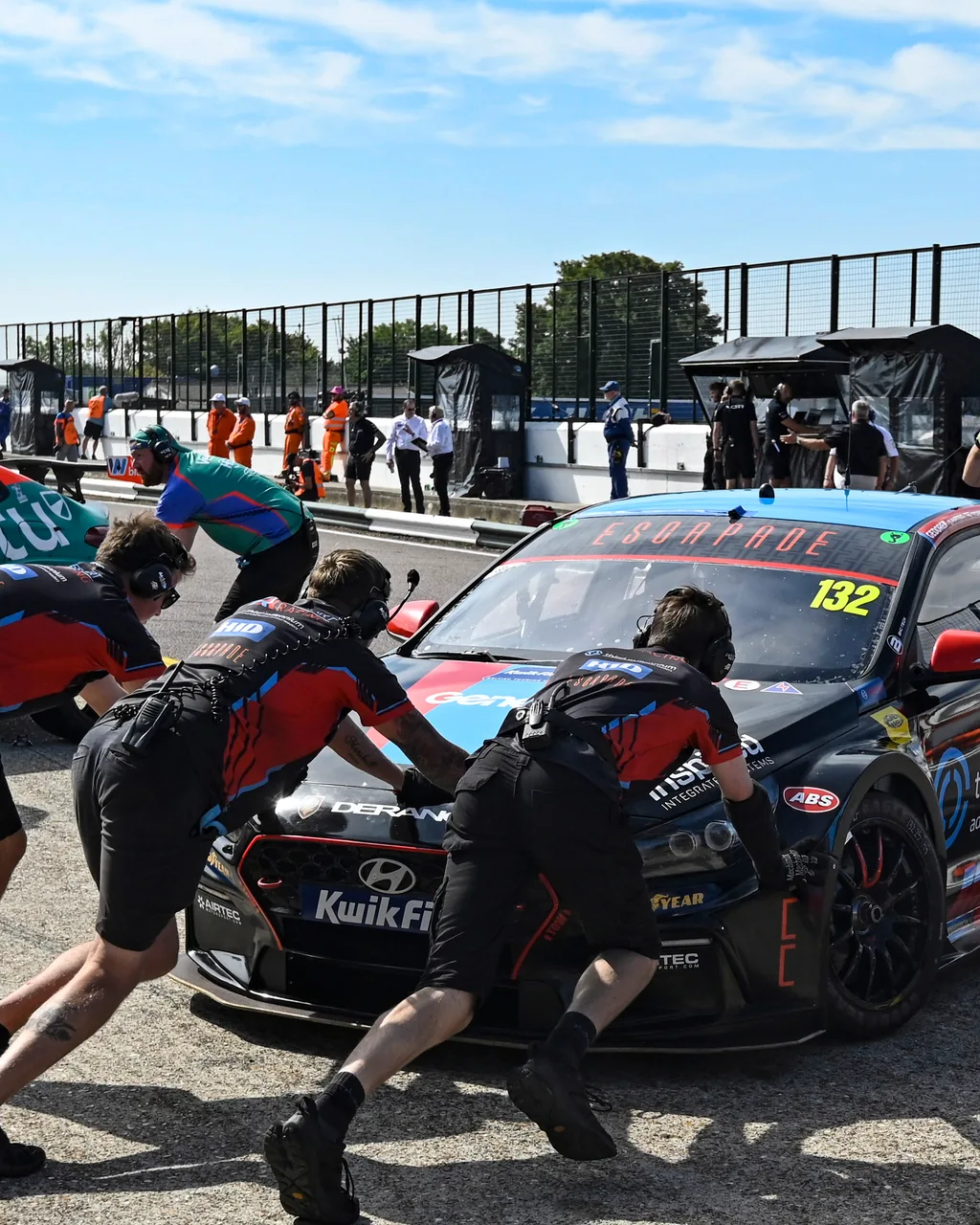 Pit crews wearing coordinated Torq teamwear push two touring cars along the pit lane.